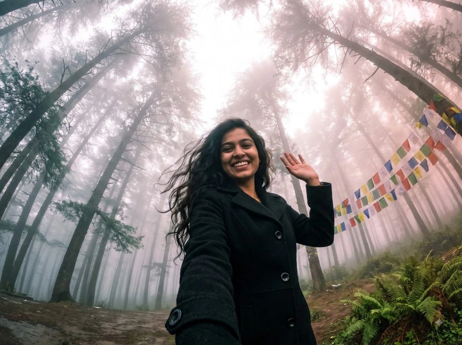 A woman in a black coat waving in a misty pine forest
